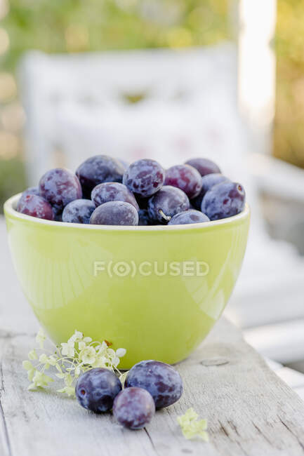 Plums in light green ceramic bowl and on wooden table — Stock Photo