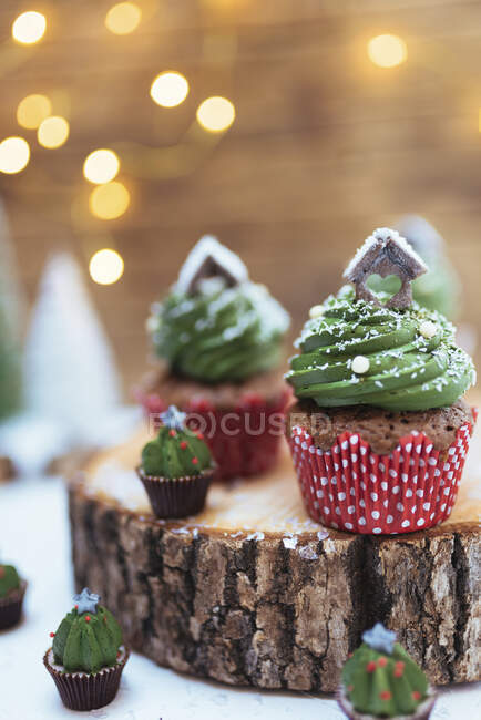 Christmas chocolate muffins with creamy green frosting on a log slice — Stock Photo