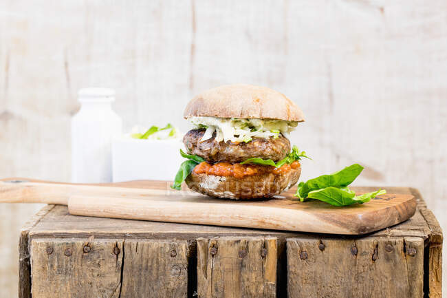 Um hambúrguer com salada de repolho numa tábua de madeira — Fotografia de Stock