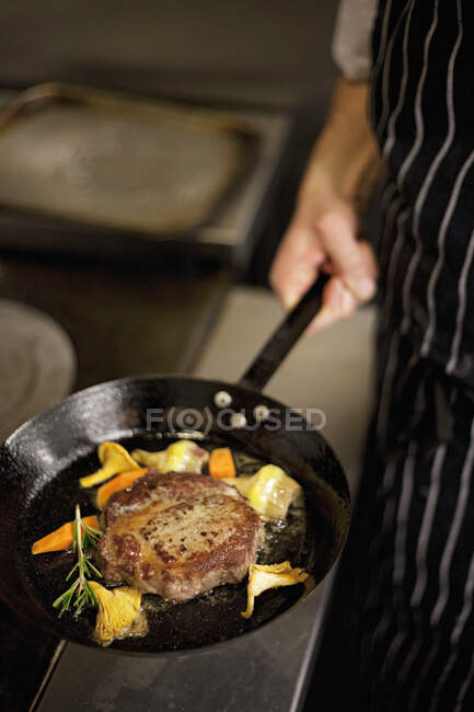 Filete de costilla con champiñones y verduras en una sartén en poder de un chef - foto de stock