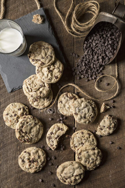 Chocolate chip cookies with glass of milk and spilled chocolate pieces — Stock Photo