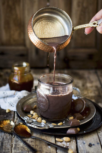 Chocolate caliente con caramelo de maní que se vierte en una taza - foto de stock