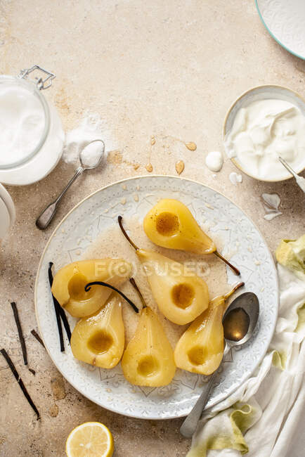 Peras escalfadas con jarabe de vainilla, cortadas a la mitad con yogur griego - foto de stock