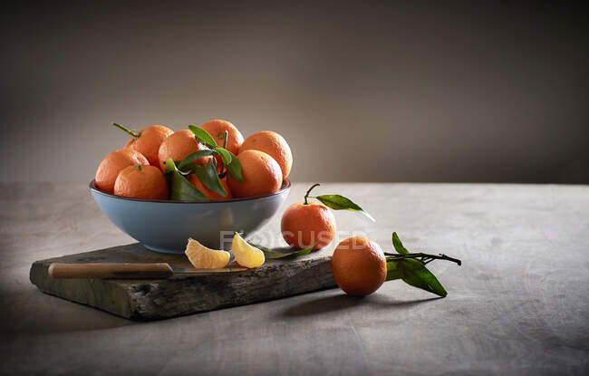 Mandarinas en un cuenco sobre una tabla de madera con un cuchillo de cocina - foto de stock