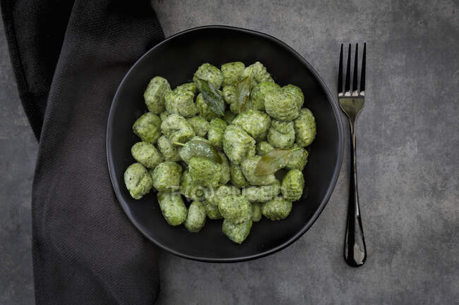 Spinach and basil gnocchi with sage in a black bowl on a grey surface — Stock Photo