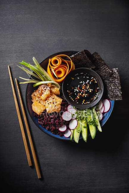 Bol de bouddha de sushi avec riz rouge, saumon, nori, légumes et sauce soja — Photo de stock