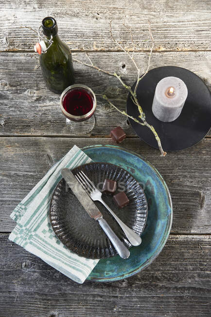 A vintage place setting with two chocolate covered marzipan and gingerbread sweets, a candle and red wine — Fotografia de Stock