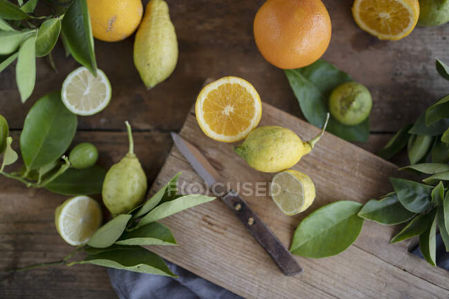 Bio-Orangen und Zitronen mit Messer auf rustikalem Holzbrett — Stockfoto