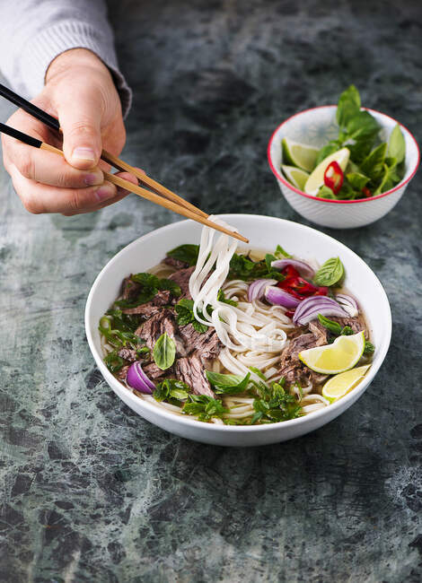 A person eating pho bo (Vietnamese beef and rice noodle soup) — Photo de stock