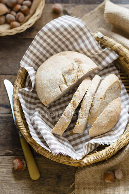 Small cut loaf of homemade bread in basket with checkered cloth — Stock Photo