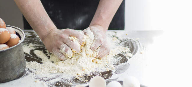 Mains pétrissant la pâte sur une surface farinée — Photo de stock