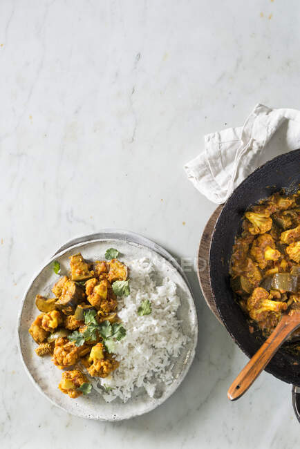 Coliflor y berenjena al curry con arroz en sartén y platos - foto de stock