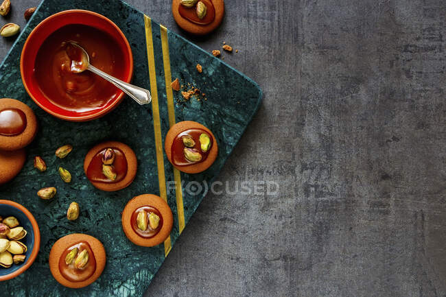 Homemade caramel and pistachio cookies on tray with nuts and topping in bowl — Stock Photo