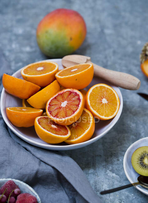 Половина окровавленных апельсинов с деревянной соковыжималкой на керамической тарелке — стоковое фото