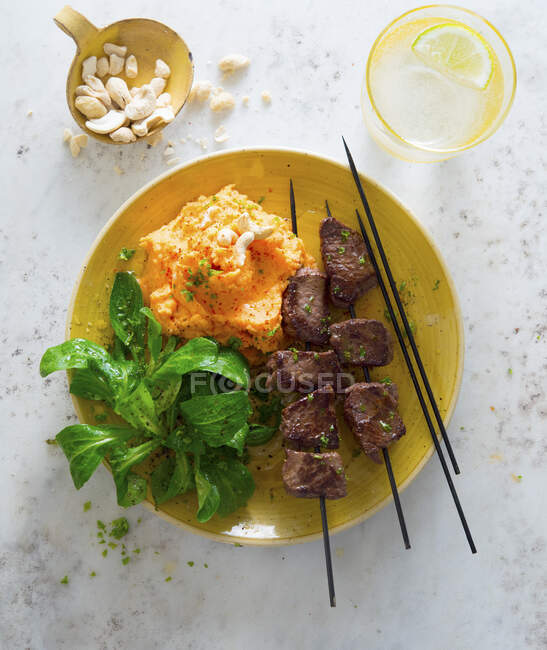 Beef skewers with mashed sweet potatoes and cashew nuts — Stock Photo