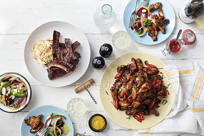 A table laid out with BBQ chicken wings, pork ribs and salad — Stock Photo
