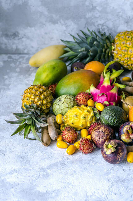 Uma grande pilha de frutas tropicais frescas e saborosas sortidas em um fundo cinza — Fotografia de Stock