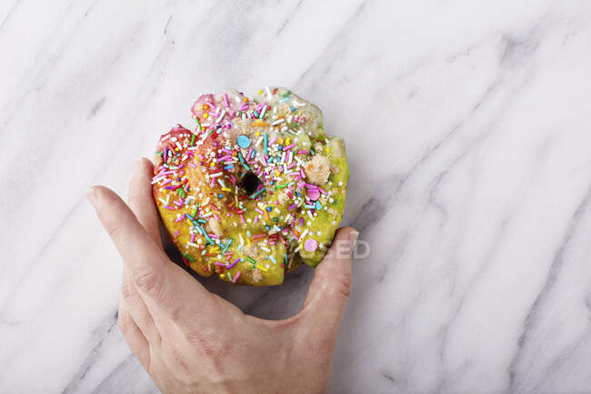Colorful and festive unicorn donut with sprinkles on marble surface with a woman s hand holding it, unicorn food trend — Stock Photo