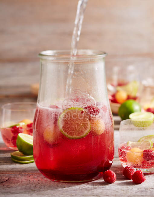 Raspberries and melon punch with champagne and limes in jar — Stock Photo