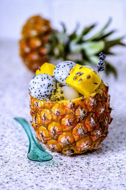 Fruit salad with various tropical fruits in a pineapple with blue transparent spoon — Stock Photo