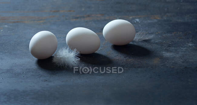 Tres huevos en la superficie oscura con plumas - foto de stock