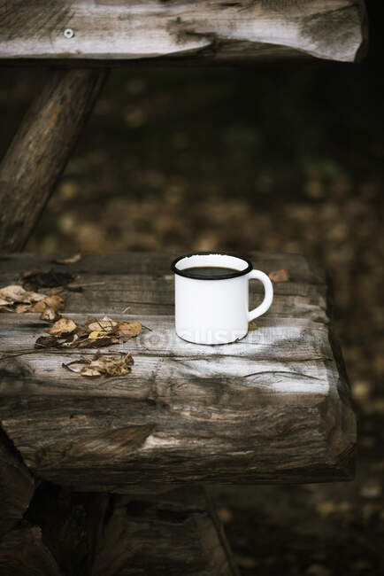 An enamel mug of coffee on a rustic wooden bench — Photo de stock
