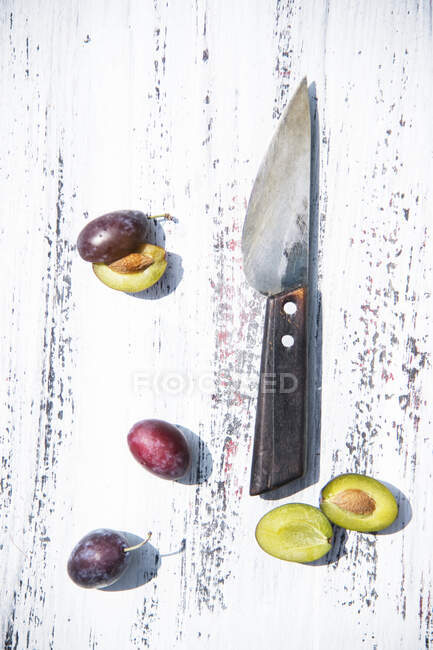 Damsons sliced and whole with a knife on a rustic wooden surface — Stock Photo