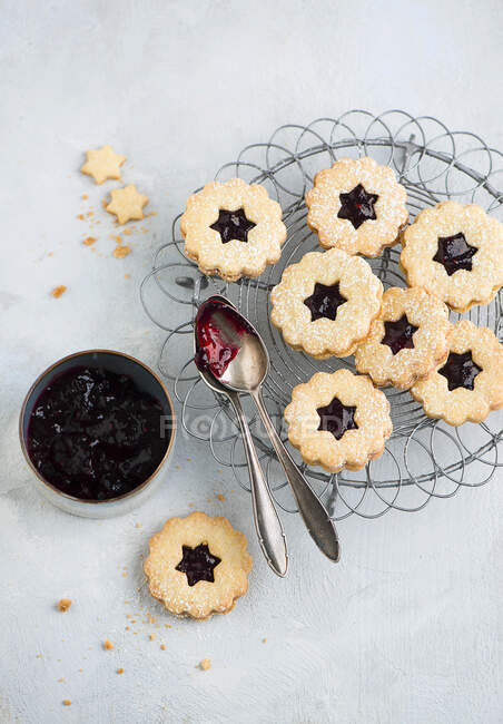 Jam sandwich biscuits on cooling rack with spoons and bowl of jam — Stock Photo