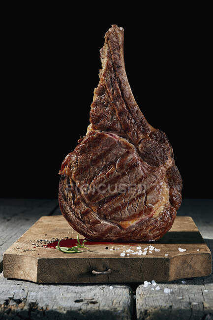 Стейк из говядины на деревянной доске на черном фоне — стоковое фото
