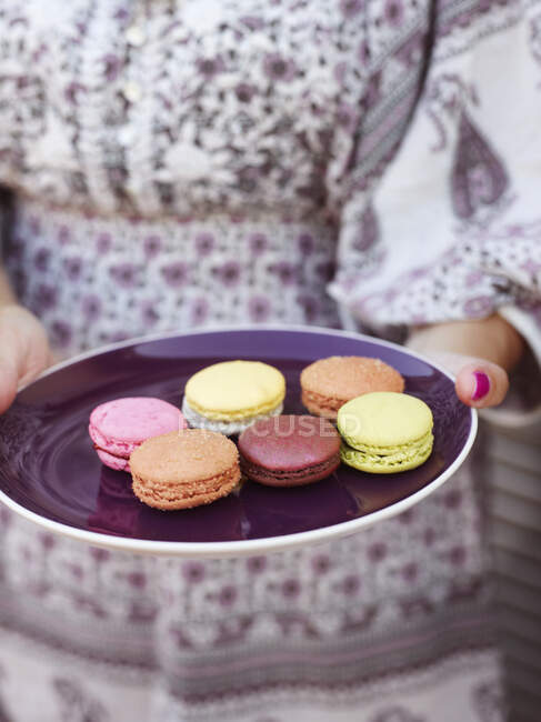Cropped shot of woman holding plate with colorful macarons — Stock Photo