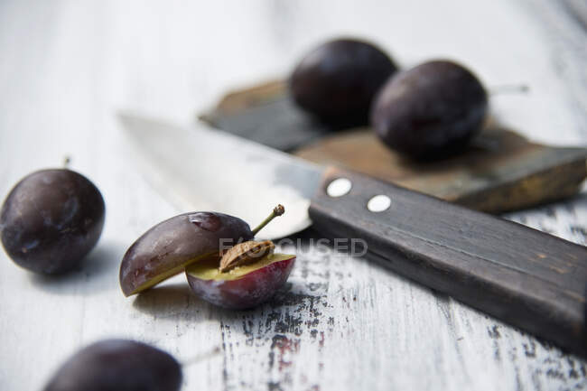 Damsons halved and whole with a knife on a rustic wooden surface — Stock Photo