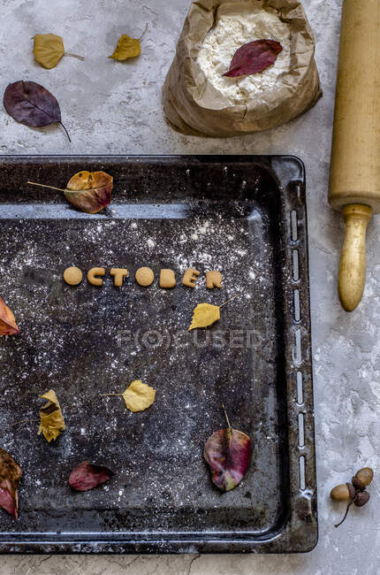 Печиво у вигляді літер, з яких викладається слово Жовтень на деку з жовтим листям — стокове фото