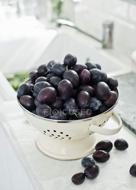 Prugne fresche in colino vintage e sul bancone della cucina — Foto stock