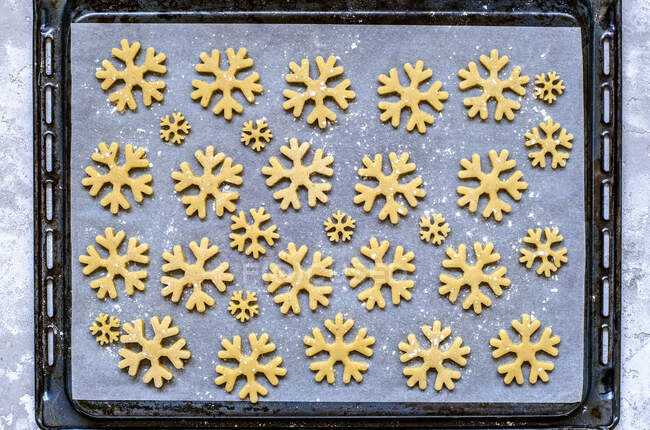 Gingerbread dough cut in snowflakes shape on parchment before baking — Stock Photo