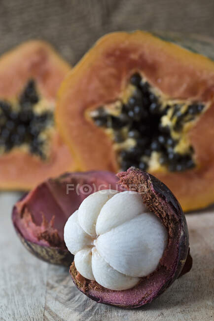 An opened mangosteen with a papaya in the background — Foto stock