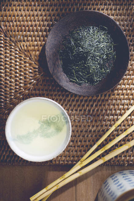 Té verde suelto en un plato y preparado en un tazón de té - foto de stock