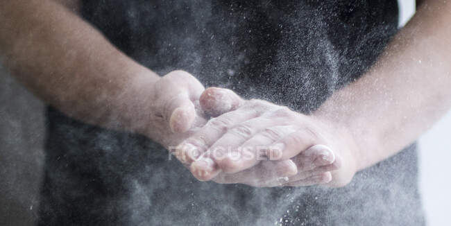 Homme au tablier noir applaudissant les mains secouant la farine — Photo de stock
