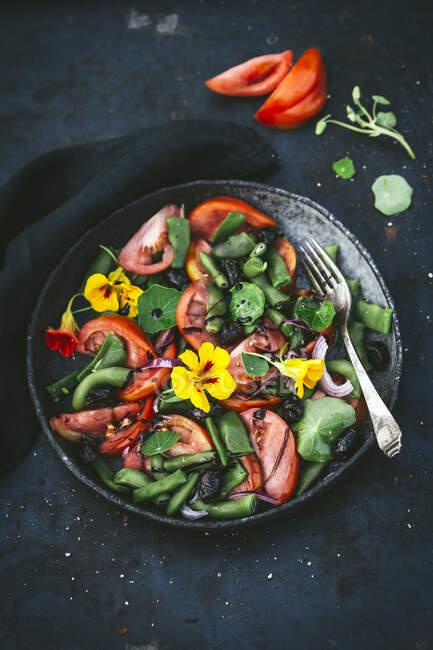 Ensalada de tomate y frijol con flores en un bol gris - foto de stock