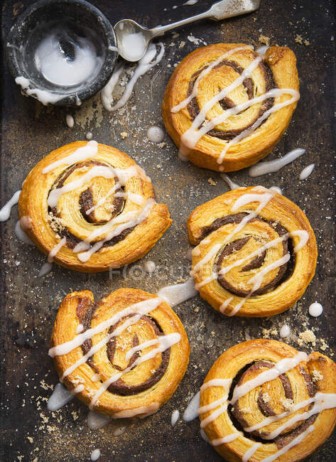 Danish Pastries cinnamon swirls on a baking tray decorated with icing — Stock Photo