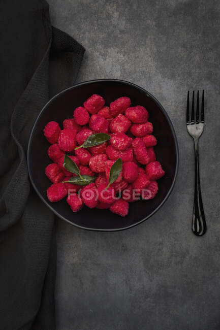 Beetroot gnocchi with sage in a black bowl on a grey surface — Stock Photo