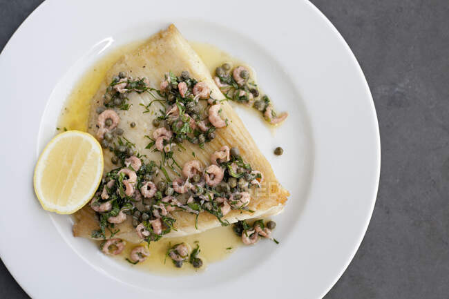 Skate wing with freshwater prawns, brownbutter, capers and a lemon wedge — Stock Photo