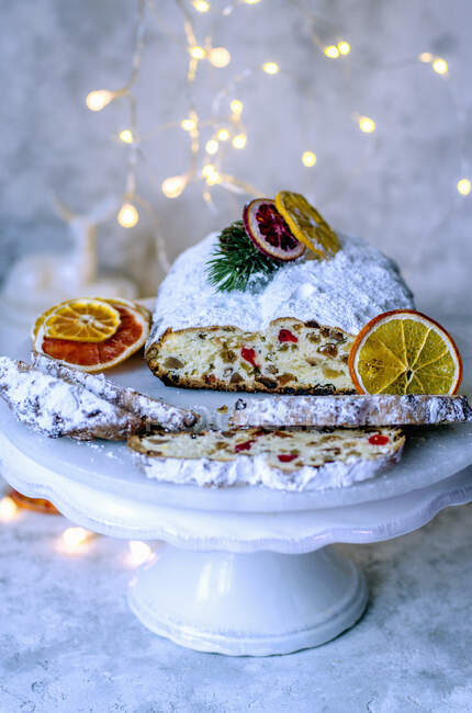 Christmas Stollen on a white stand decorated with dry slices of orange and garland — Stock Photo