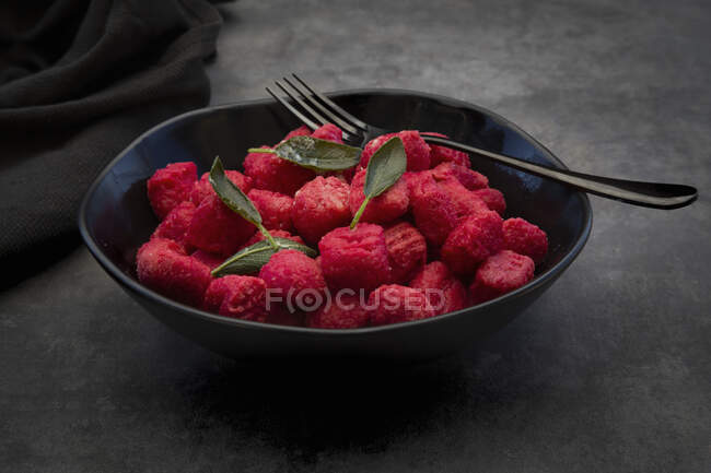 Beetroot gnocchi with sage in a black bowl — Stock Photo