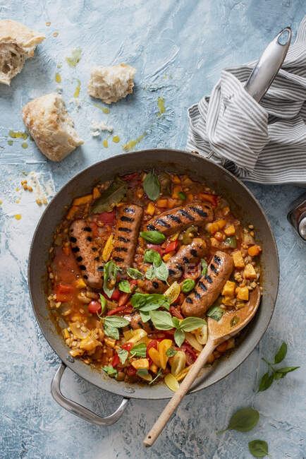 Une casserole de saucisses de style chorizo avec orge perlé, patates douces, tomates et basilic — Photo de stock