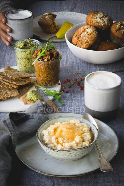 Haferbrei mit Birnenkompott, Cracker, Tomaten-Kürbis-Dip, Birnenmuffins und einem Latte zum Frühstück — Stockfoto