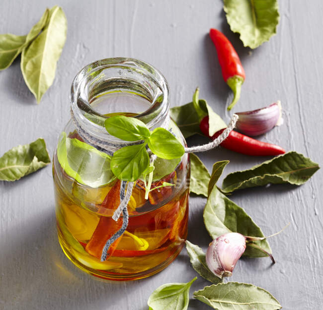 Aceite de albahaca-laurel con ajo y peperoncini en un frasco pequeño - foto de stock