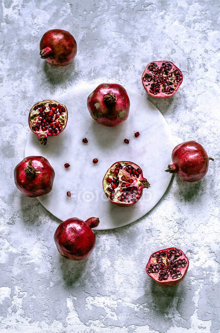 Fresh pomegranates whole and cut with scattered grains on a marble tray — Stock Photo