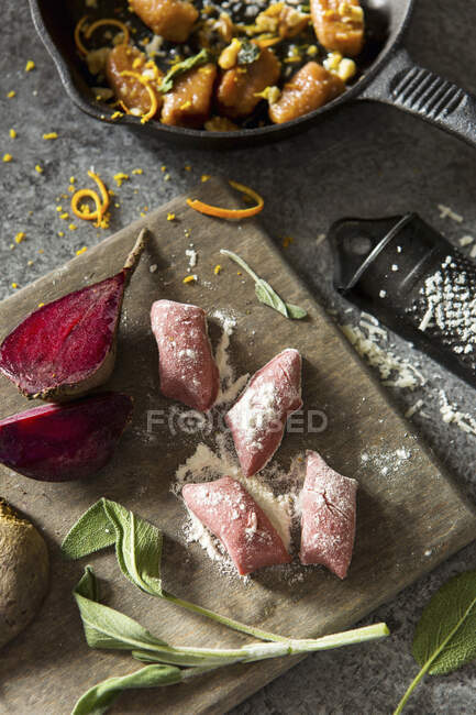 Nhoque de beterraba em uma tábua de cortar com sálvia fresca, beterraba crua, parmesão e prato cozido — Fotografia de Stock