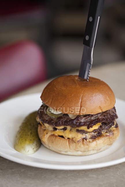 Hambúrguer de queijo duplo em uma chapa com um pepino — Fotografia de Stock