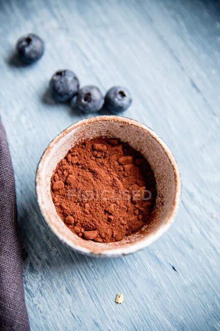 Poudre de cacao en tasse et bleuets sur la surface en bois — Photo de stock